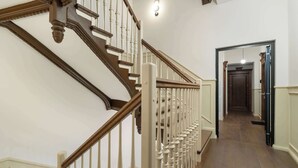Een trap met houten spijlen en een leuning, die leidt naar een gang met een houten vloer en een deur aan het einde.