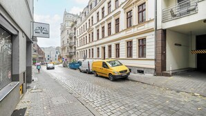 A cobblestone street lined with historic buildings, a yellow van parked on the side, and a person walking with an umbrella. - Spacious Apartment in the Center | Two Bedrooms | Desk. (Poznań)