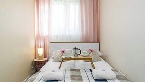 Habitación de hotel ordenada con una cama, una mesita de noche con lámpara, y una bandeja con cafetera, tazas y tetera.