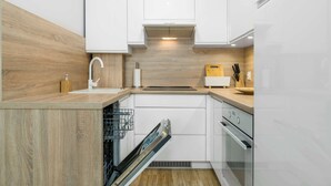 Una cocina moderna con armarios blancos, encimera de madera, lavavajillas integrado y horno.