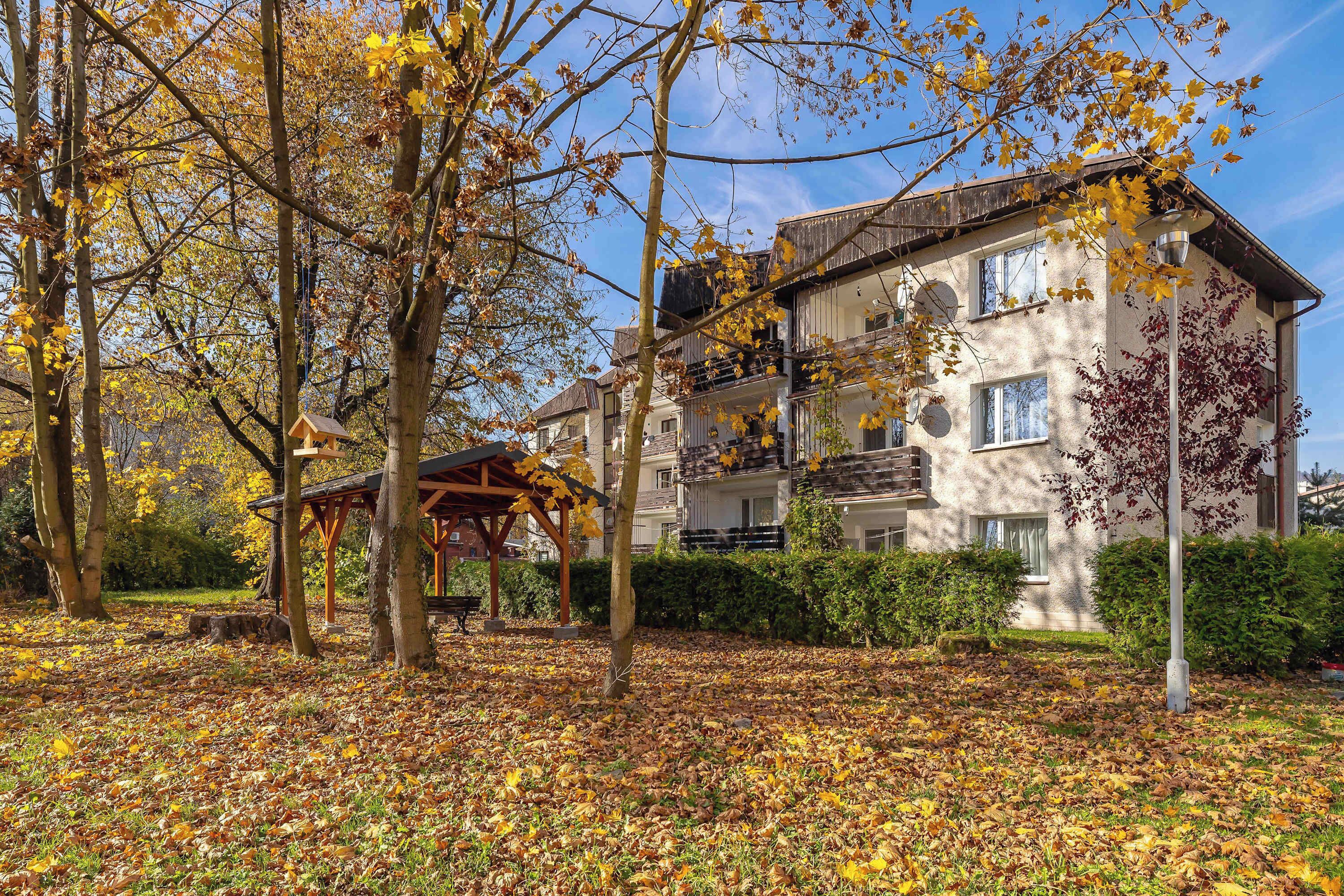 Un immeuble à plusieurs étages doté d’un jardin, d’un belvédère et d’un banc.