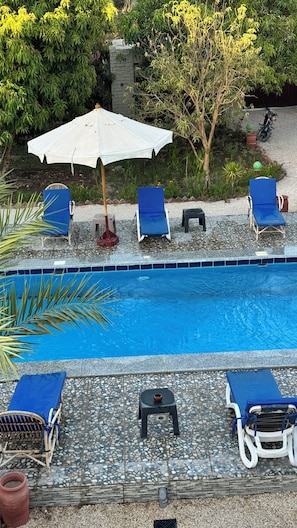 Una piscina con poltrone da relax blu e un ombrellone bianco.