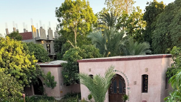 A pool area with lounge chairs, a table, and a building with a pink facade. - Ramses Villa in ElJuneina Villas (Luxor)