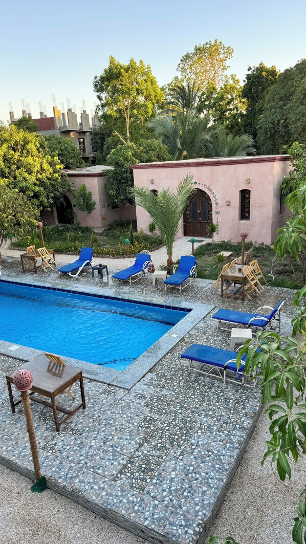 Un área de piscina con sillones de descanso, una mesa y un edificio de fachada rosa.