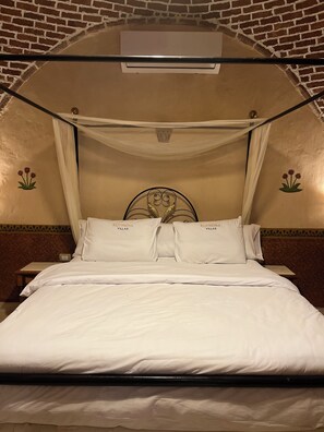 Un lit avec du linge de lit blanc, un baldaquin et une tête de lit ornée de motifs floraux.