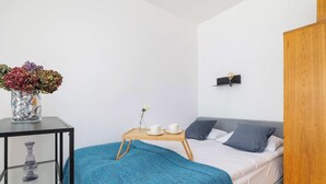 Quarto com cama, mesa de cabeceira com um vaso, bandeja com xícaras e prateleira na parede.