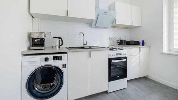 Cozinha compacta com máquina de lavar, cafeteira, micro-ondas e fogão.