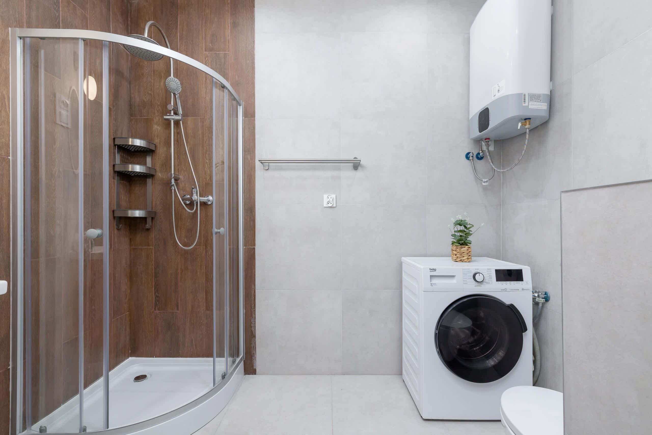 A modern bathroom with a glass-enclosed shower, a built-in washing machine, and a wall-mounted air conditioner.