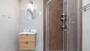 Une salle de bain moderne avec une douche à parois de verre, un meuble-lavabo en bois et un miroir rond doté d’un luminaire.