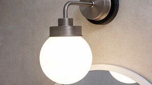Un luminaire mural doté d’une ampoule ronde, d’un bras incurvé et d’un socle métallique.