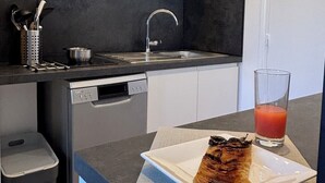 A modern kitchen with white cabinets, a black backsplash, a stainless steel sink, and a dishwasher. A plate with food and a glass of red drink are on the counter. - Magnificent apartment on the outskirts of St Tropez (Cogolin)
