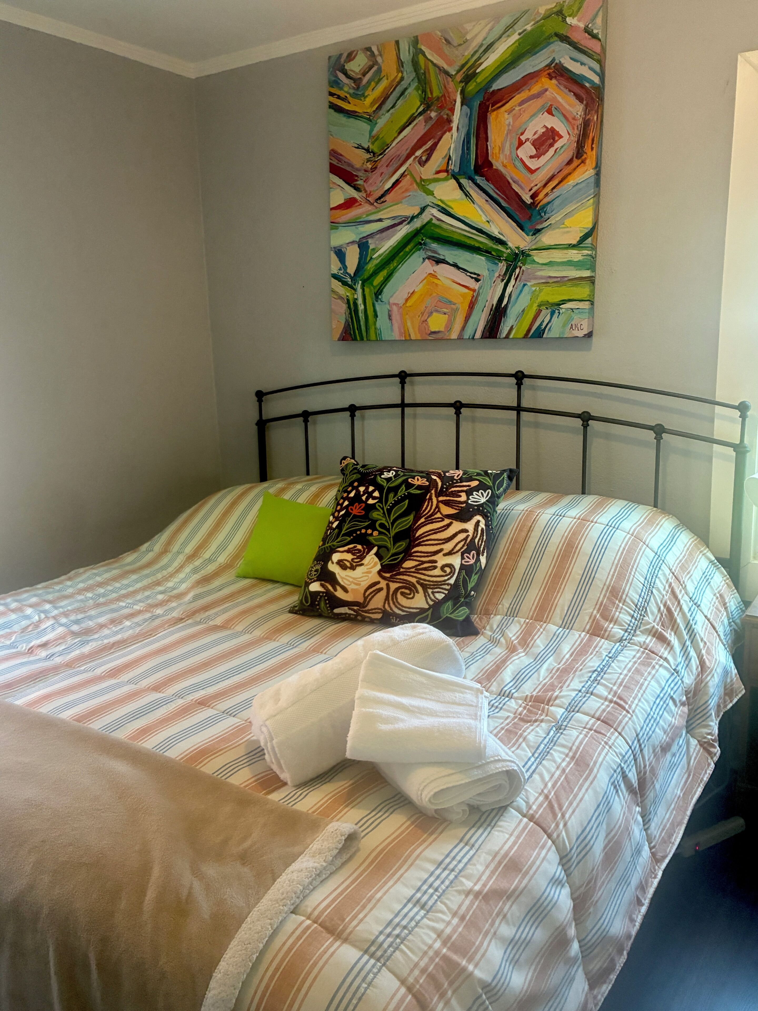 A bed with striped bedding, a green pillow, and a colorful abstract painting on the wall.