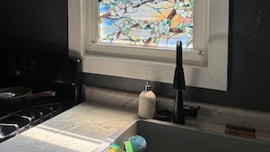 A kitchen with a window featuring a stained glass design, a sink with dish racks, and a stove.