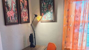 Un bureau d’angle comprenant un bureau, une chaise, une lampe et deux tableaux encadrés accrochés au mur.