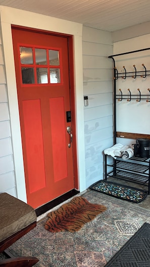 A red door with a keypad lock, a black coat rack with hangers, a bench, and a patterned rug.
