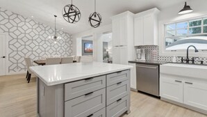 A modern kitchen with white cabinetry, a large island with drawers, pendant lighting, and a view of the outdoors through a window. - Scottsdale Oasis | Heated Pool | Spa | Grill (Scottsdale)