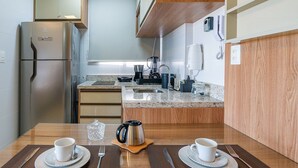Une cuisine moderne équipée d’un réfrigérateur, d’une machine à café et d’une table à manger avec des tasses et des couverts.