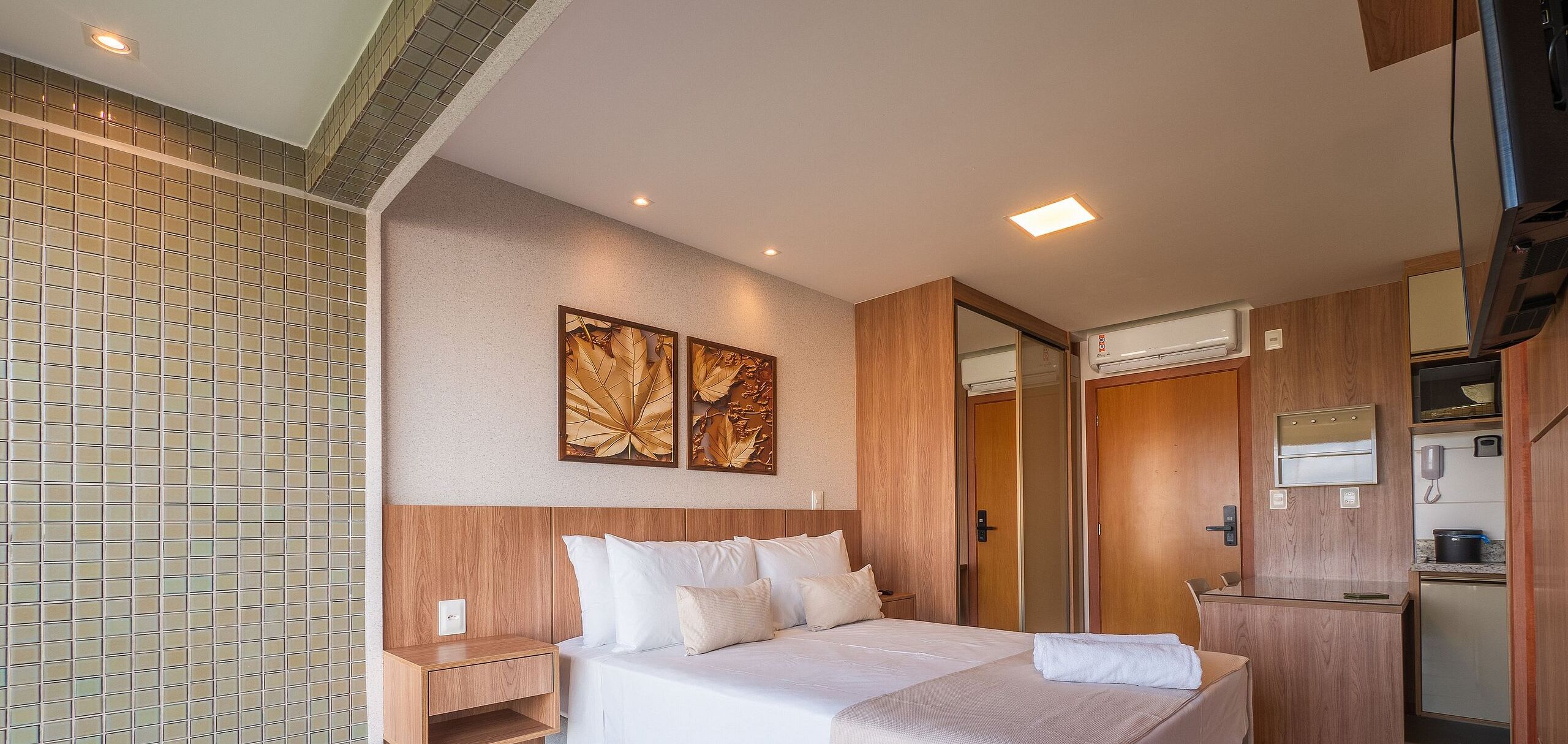 Ein Hotelzimmer mit Bett, Nachttisch, Wand-Klimaanlage und einer kleinen Küchenzeile.