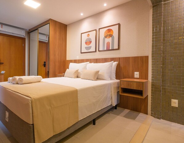A hotel room with a bed, a bedside table, a wall-mounted artwork, and a tiled shower wall. - Comfortable Studio in Caminho das Árvores (Salvador)