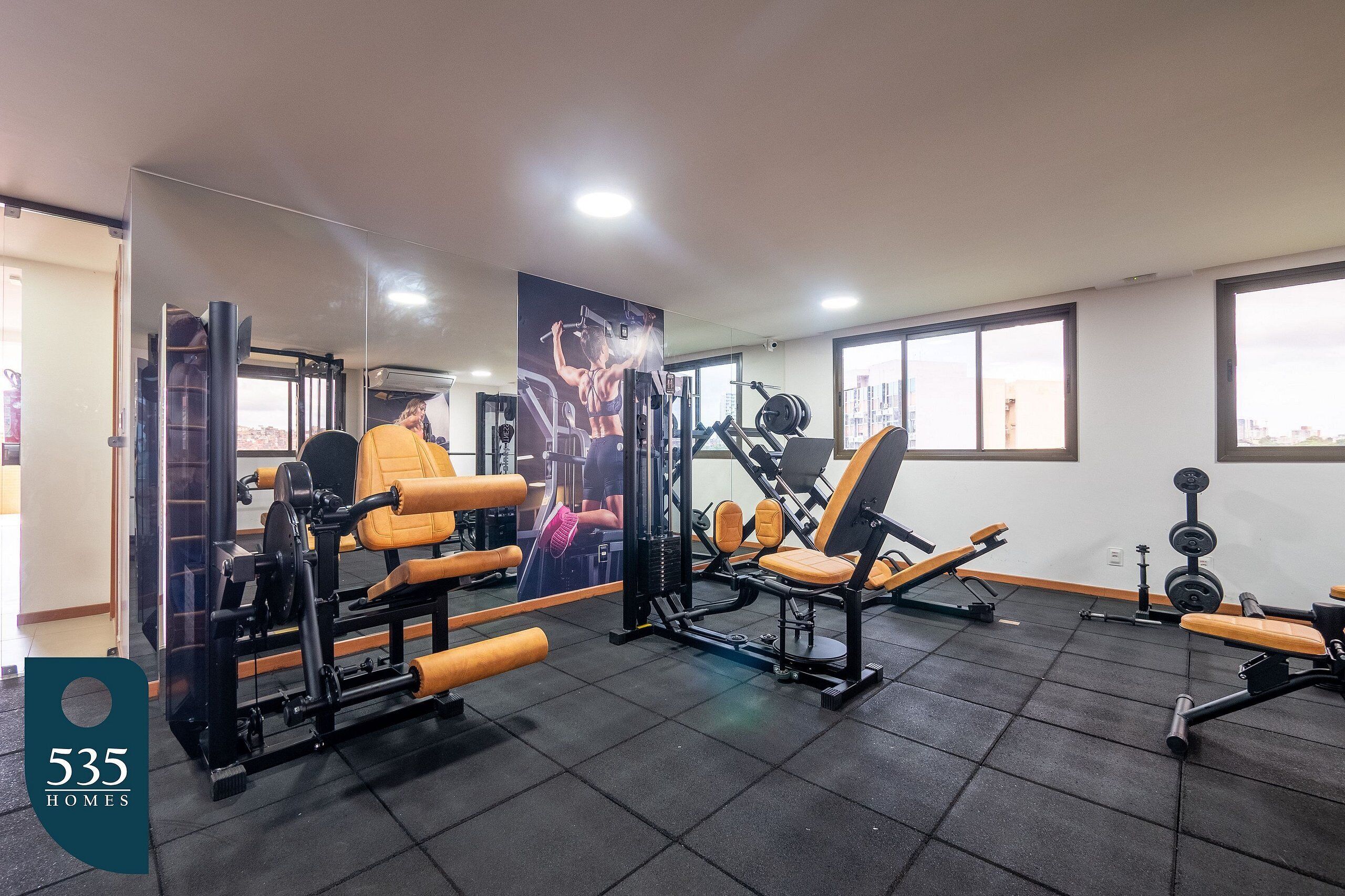 A gym with various exercise machines, a large mirror, and a view of the city through large windows.