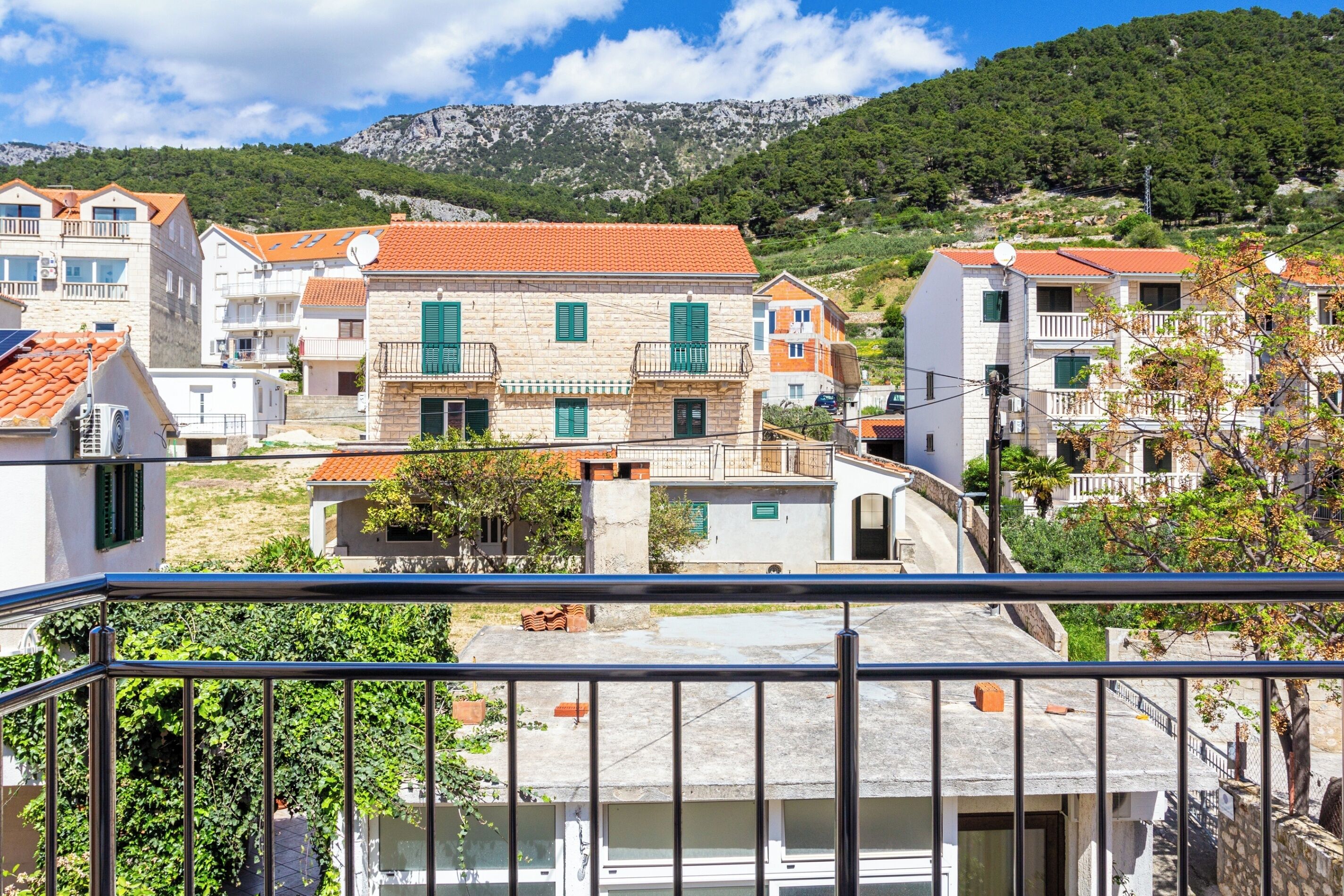 A coastal residential area with stone buildings, balconies, and a mountainous backdrop.