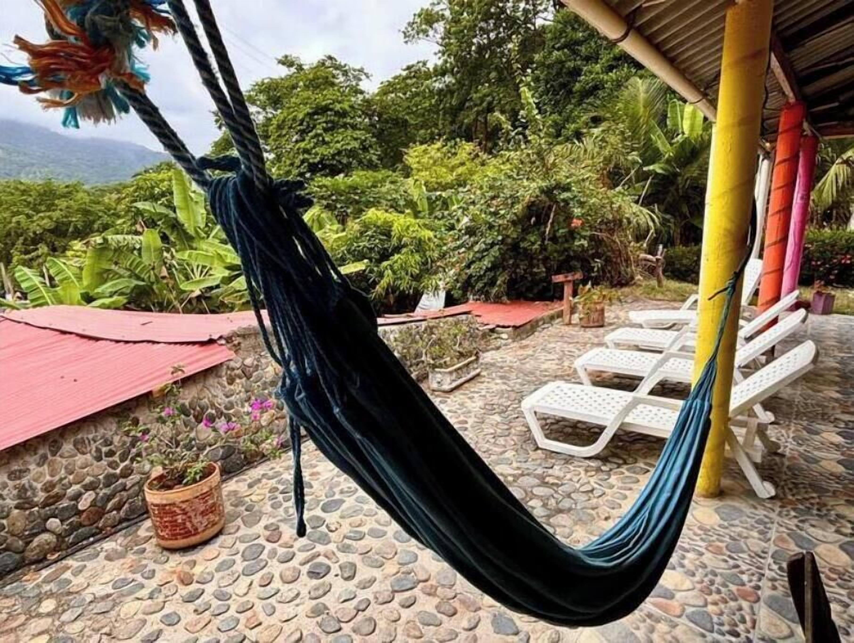 Una hamaca colgada entre dos postes, con un patio empedrado y sillones blancos al fondo.