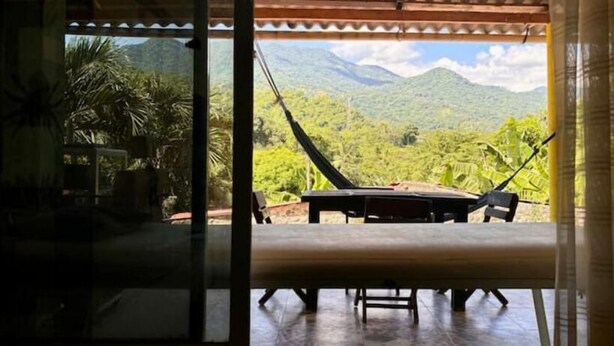 Poltrona suspensa e mesa montadas numa varanda com vista para vegetação exuberante e montanhas.