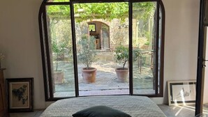 Una camera da letto con un'ampia finestra che si affaccia su un cortile con piante in vaso e una struttura in legno.