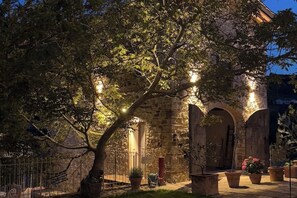 Ein Steinhaus mit Rundbogenportalen und einem Baum im Vordergrund.