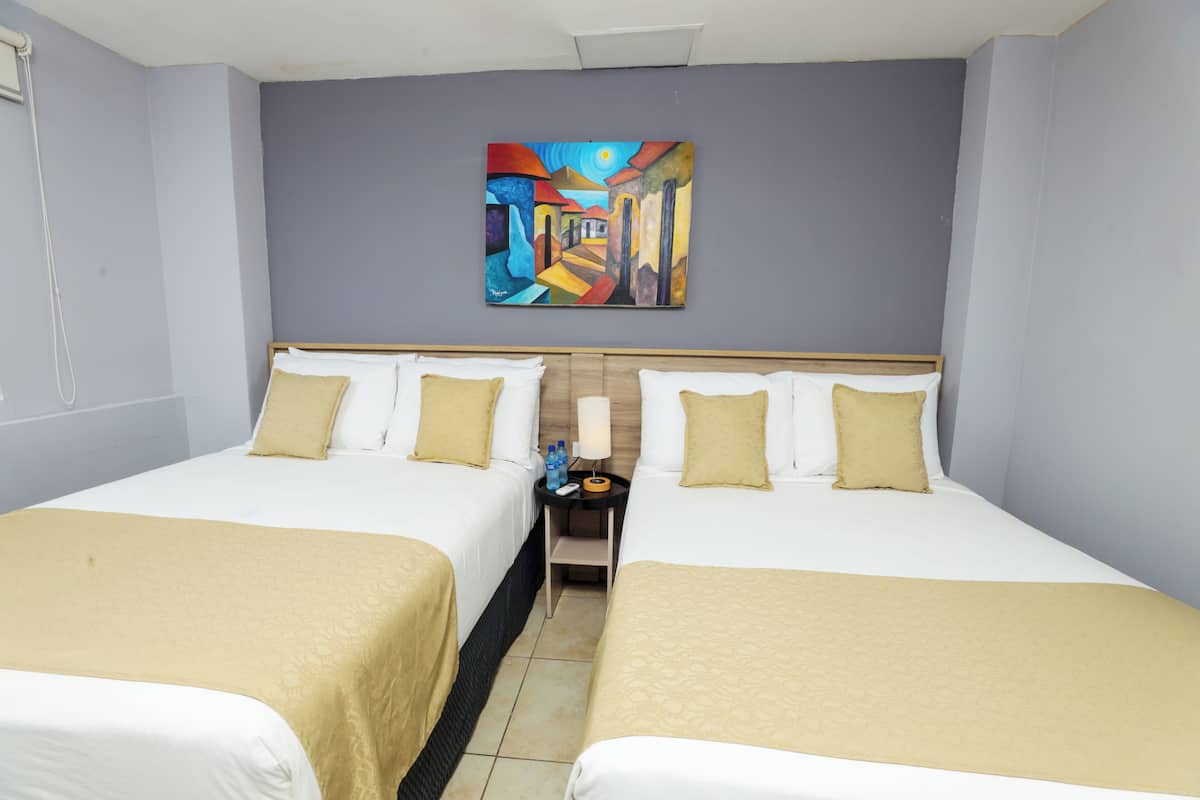Habitación de hotel con dos camas, ropa de cama color beige, una mesita de noche con lámpara y un cuadro abstracto de colores en la pared.