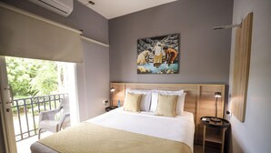 Une chambre d’hôtel avec un grand lit, un tableau au mur, une table de chevet et un balcon avec des chaises.
