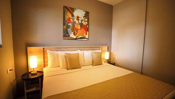 A hotel room with a large bed, two bedside tables with lamps, a painting on the wall, and a plain wall.