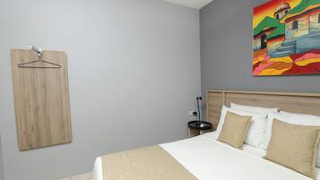 A bedroom with a bed, a wooden hanger, a nightstand, and a painting on the wall.