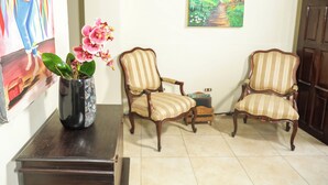 Une pièce comprenant deux fauteuils rembourrés, une table en bois, un vase avec des fleurs roses, un tableau accroché au mur et une porte.