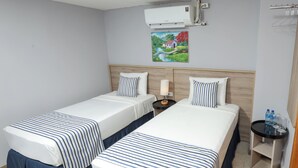 Une chambre d’hôtel avec deux lits, une table de chevet, un climatiseur, un tableau et une petite table avec des bouteilles d’eau.
