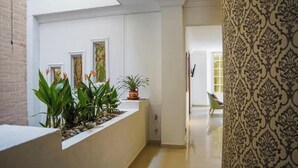 A hallway with a white wall, a plant display, and a patterned curtain.