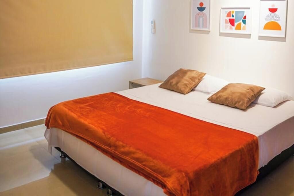 A neatly made bed with a white and orange bedspread, two pillows, and a bedside table with a lamp.