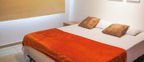 A neatly made bed with a white and orange bedspread, two pillows, and a bedside table with a lamp.