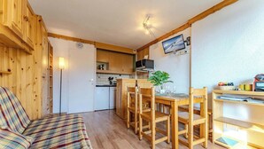 Acogedor interior de cabaña con un sofá de cuadros, una mesa de comedor de madera, sillas, una zona de cocina y un televisor montado.