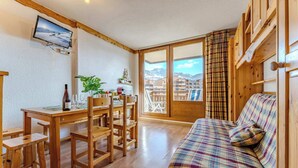 Una sala de estar acogedora con una mesa de comedor de madera, sillas, un sofá con tapicería escocesa y un ventanal con vistas a la montaña.
