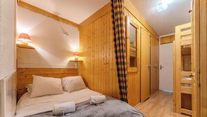 Un dormitorio acogedor con cabecera de madera, cama con ropa de cama blanca, mesita de noche con lámparas y cortina a cuadros.