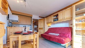 Una habitación acogedora con una mesa de comedor de madera para cuatro personas, un sofá rojo y armarios de madera con puertas de cristal.