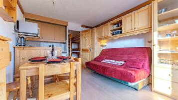A cozy room with a wooden dining table set for four, a red sofa, and wooden cabinets with glass doors.