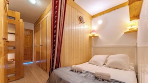 Una habitación de madera con una cama, un armario y una pequeña mesa con botellas.