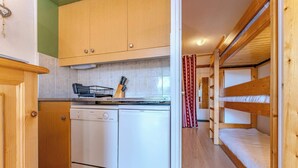 Cocina compacta con armarios de madera, lavavajillas y encimera con escurreplatos y utensilios.