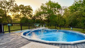 An outdoor swimming pool with a wooden deck, surrounded by a black fence and trees. - Beautiful country home escape for a Country Christmas in Bellville, TX (Bellville)