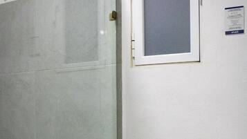 Un baño con cabina de ducha de vidrio, inodoro y una pequeña ventana sobre el inodoro.