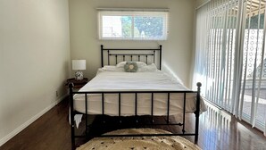 A bedroom with a bed, a ceiling fan, a window with blinds, and a large woven rug.