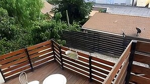 A wooden deck with two white chairs and a small table, surrounded by a wooden fence and greenery.