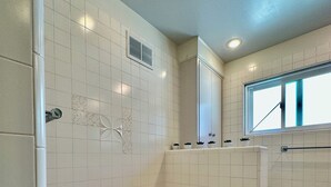 A bathroom with a large bathtub, white tiled walls, a window, and a shower area.